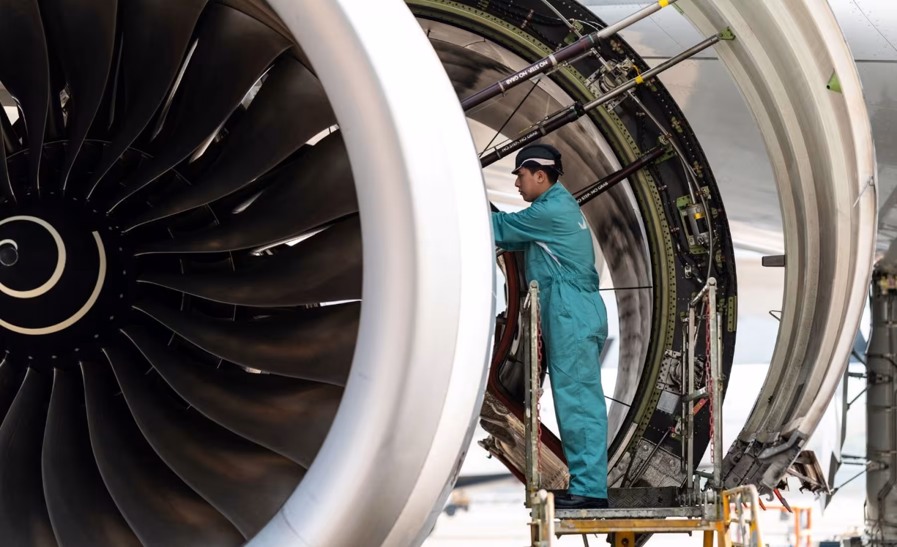 Aircraft engine maintenance technician inspecting a jet engine on a maintenance platform.