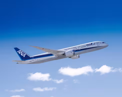 ANA passenger aircraft climbing after take-off, shown in side view against a clear blue sky with a few scattered clouds.