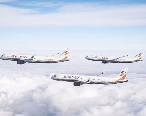 Three STARLUX Airlines aircraft flying in formation above the clouds under a blue sky.