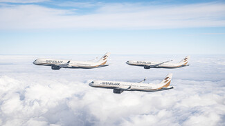 Three STARLUX Airlines aircraft flying in formation above the clouds under a blue sky.